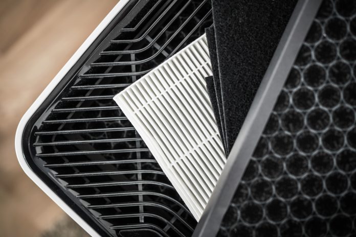 Close-up of a pleated HEPA filter panel being removed from an air purifier, showing the filter media and activated carbon layer