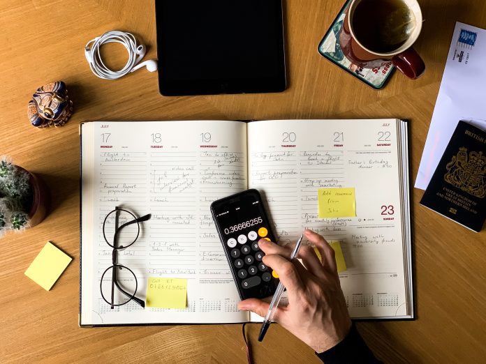Hand using a calculator with a planner on a desk