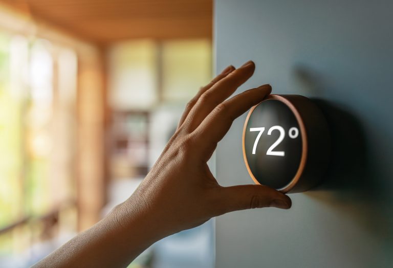 Hand adjusting a smart thermostat in a sunlit home