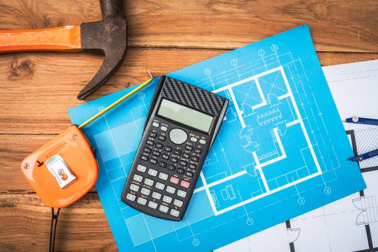 Calculator, measuring tape, and blueprint on a desk