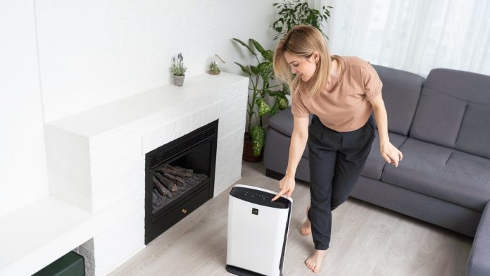 Woman operating a white air purifier in a sunlit living room to control household dust